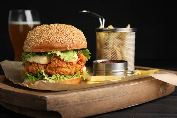 Delicious burger with crispy chicken patty, french fries and sauce on table