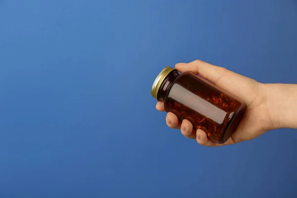 Woman holding jar with vitamin capsules on blue background, closeup. Space for text