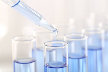Laboratuvar analizi. Pipetten açık mavi sıvıyı bulanık arkaplanda cam test tüpüne damlatarak, yakın plan