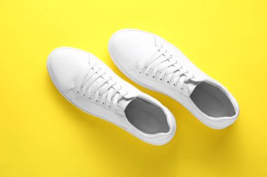Sarı arka planda bir çift şık beyaz spor ayakkabı.