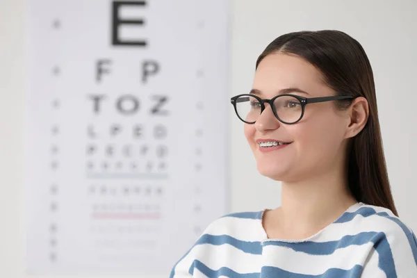Young woman with glasses against vision test chart
