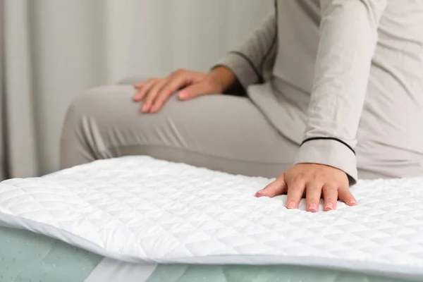 Woman sitting on new soft mattress indoors, closeup