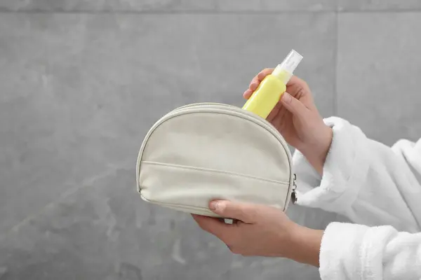 Woman packing cosmetic travel kit near grey wall closeup and space for text. Bath accessories
