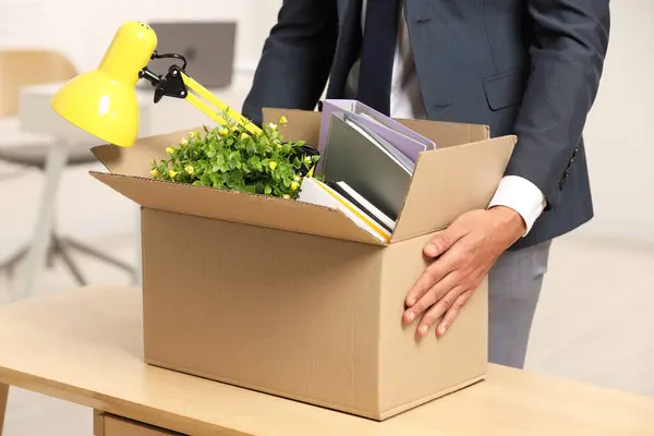 Unemployment problem. Man with box of personal belongings at table in office, closeup