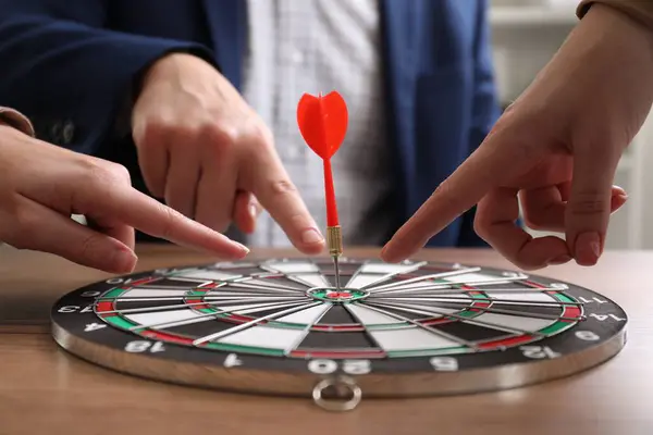 Business targeting concept. People pointing at dartboard at table, closeup