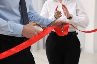 Kırmızı kurdeleyi içeride makasla kesen adam, yakın plan.