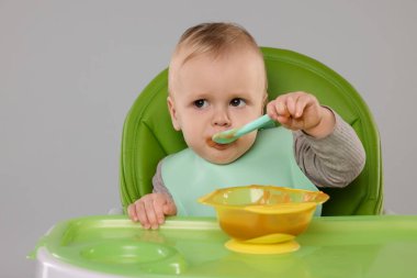 Küçük şirin bebek sağlıklı yiyecekler yiyor arka planda gri sandalyede, mesaj atmak için yer var.