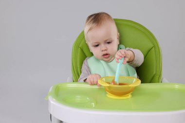 Küçük şirin bebek sağlıklı yiyecekler yiyor arka planda gri sandalyede, mesaj atmak için yer var.