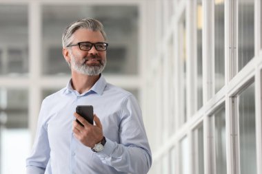 Ofisinde akıllı telefonu olan gülümseyen bir adam, düşük açı. Avukat, işadamı, muhasebeci ya da yönetici.