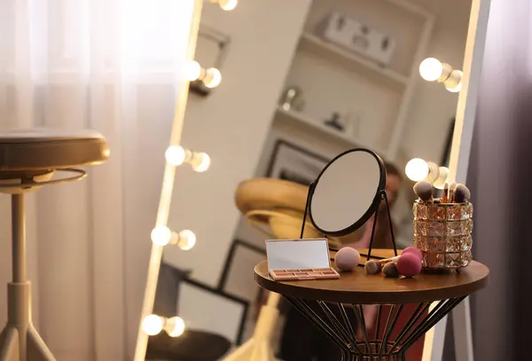 Makeup room. Stylish mirror with light bulbs and beauty products on wooden table indoors