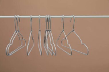 Boş giysiler açık kahverengi arka planda askıda asılı.