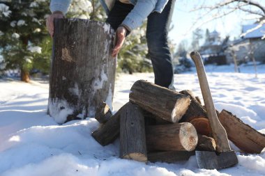 Adam kütüğü doğramaya hazırlanıyor, yakın plan. Kar üzerine balta ve kütük yığını, seçici odaklanma