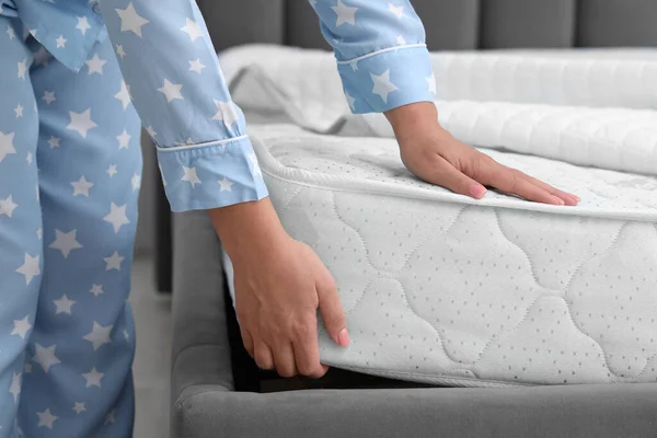 Woman putting new soft mattress on grey bed indoors, closeup