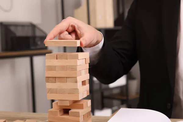 Playing Jenga. Man building tower with wooden blocks at table indoors, closeup