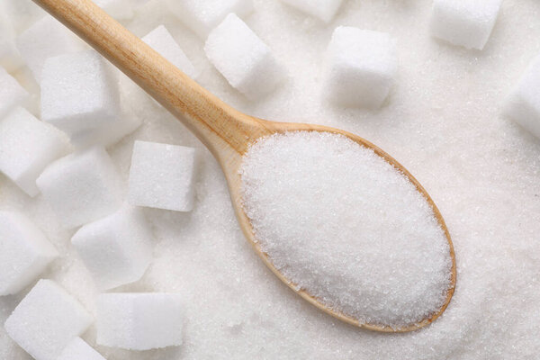 Different types of white sugar and spoon as background, top view