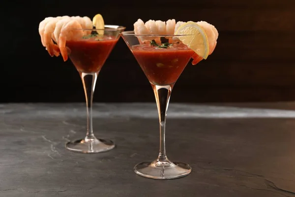Tasty shrimp cocktail with sauce in glasses and lemon on grey textured table