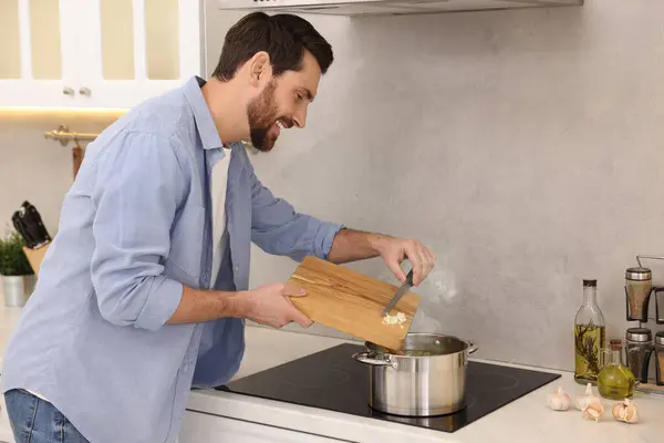 Man adding garlic into soup in kitchen
