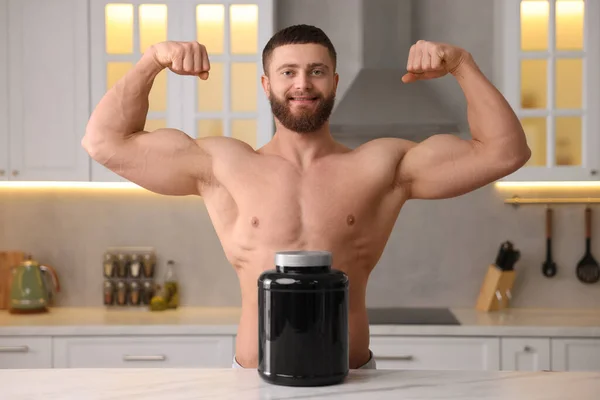 Young man with jar of protein powder at white marble table in kitchen