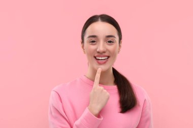 Güzel bir kadın temiz dişlerini gösteriyor ve pembe arka planda gülümsüyor.