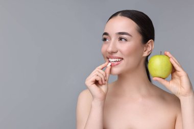Vitamin hapı ve gri arka planda elması olan güzel bir genç kadın. Metin için boşluk