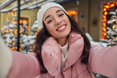 Kışın şehrin sokaklarında selfie çeken gülümseyen kadın portresi.