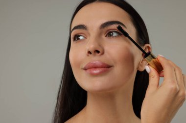 Gri arka planda rimel süren güzel genç bir kadın. Yakın plan.