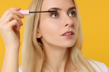 Güzel bir kadın turuncu arka plana rimel sürüyor, yakın plan.