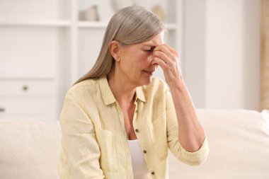Menopoz. Evdeki kanepede baş ağrısı çeken bir kadın.