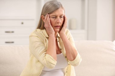 Menopoz. Evdeki kanepede baş ağrısı çeken bir kadın.