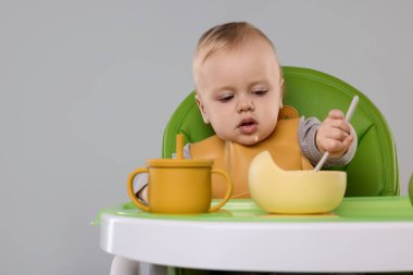 Küçük şirin bebek sağlıklı yiyecekler yiyor arka planda gri sandalyede, mesaj atmak için yer var.