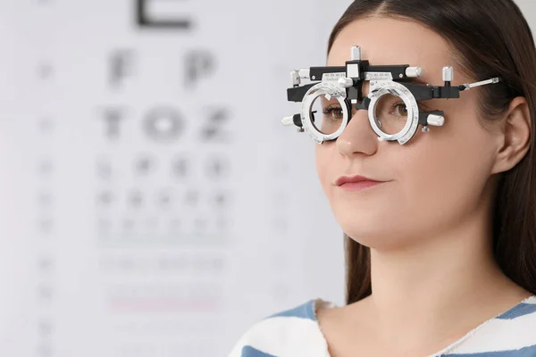 Young woman with trial frame against vision test chart