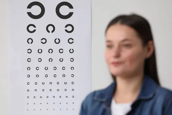 Young woman against vision test chart, selective focus