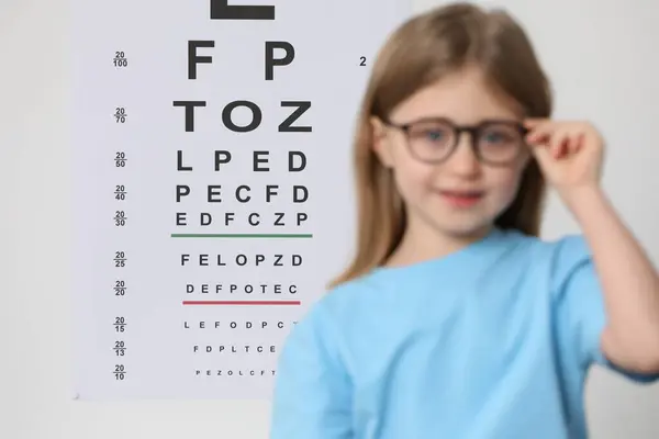 Little girl with glasses against vision test chart, selective focus