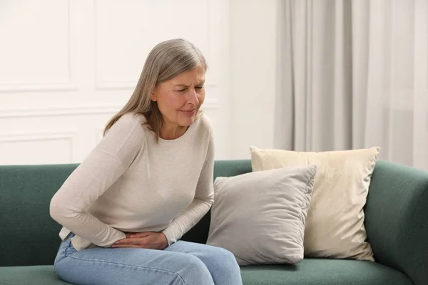 Menopause. Woman suffering from abdominal pain on sofa at home