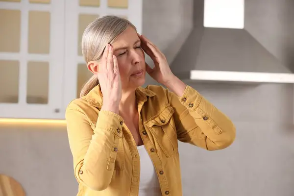 Menopause. Woman suffering from headache in kitchen