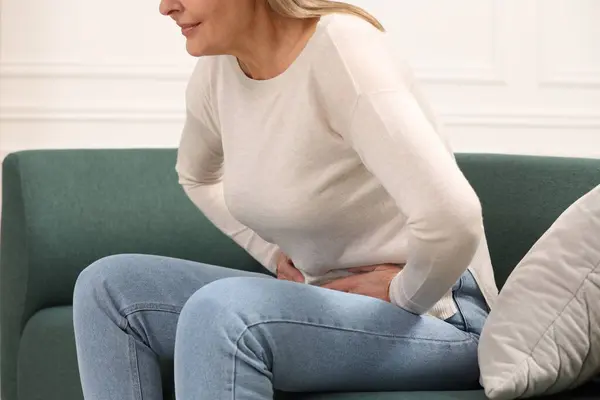 Menopause. Woman suffering from abdominal pain on sofa at home, closeup