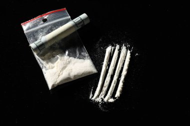 Uyuşturucu bağımlılığı. Kokain dolu plastik torba ve siyah arka planda yuvarlanmış dolar banknotu.