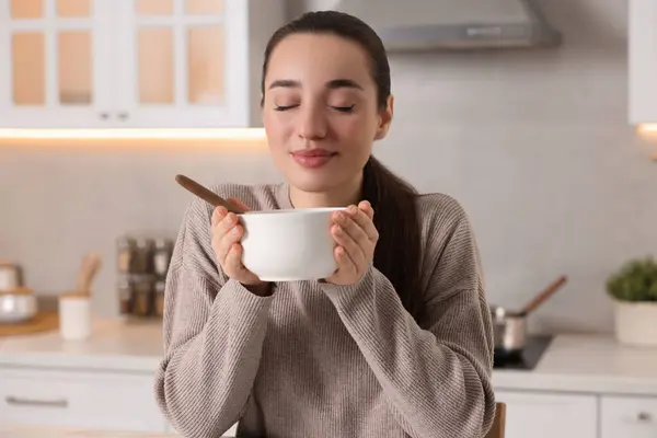 Woman with bowl of tasty soup in kitchen