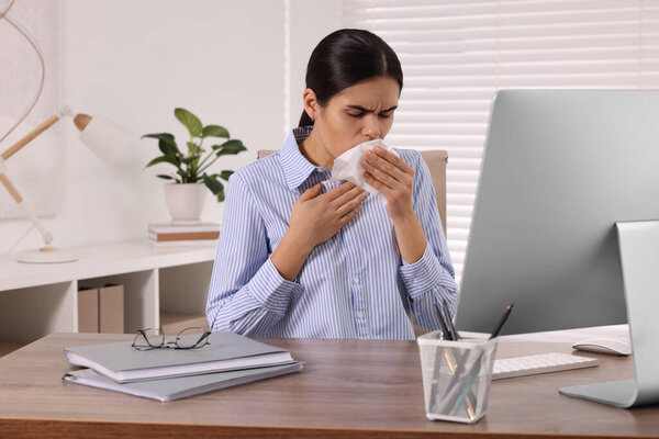 Woman with tissue coughing at table in office. Cold symptoms