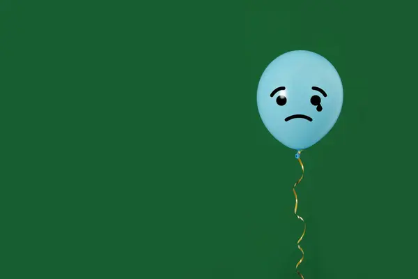 Light blue balloon with sad face on green background. Space for text