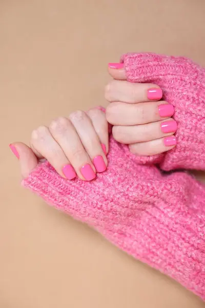 Woman showing her manicured hands with pink nail polish on dark beige background, top view