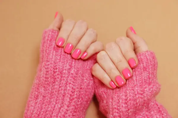 Woman showing her manicured hands with pink nail polish on dark beige background, closeup