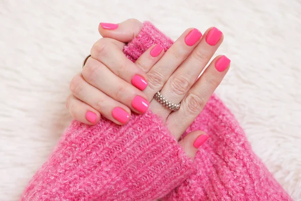 Woman showing her manicured hands with pink nail polish on faux fur mat, closeup
