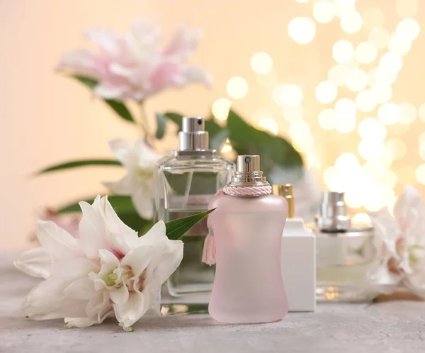 Perfume bottles and bouquet of beautiful lily flowers on table against beige background with blurred lights, closeup