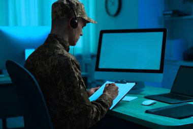 Askerlik. Pano ve kulaklıklı bir asker. Geceleri ofisteki ahşap masada çalışıyor.