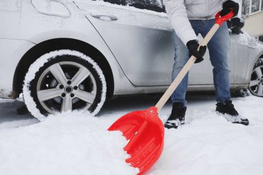 Adam arabanın yanında kürekle karları kaldırıyor, yakın plan.