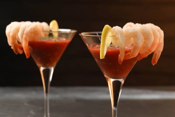 Tasty shrimp cocktail with sauce in glasses and lemon on grey table, closeup