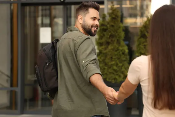Long-distance relationship. Man with backpack holding hands with his girlfriend near building outdoors