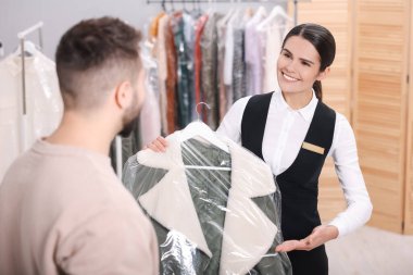 Kuru temizleme servisi. Mutlu işçi içeride müşteriye plastik torba içinde palto veriyor.