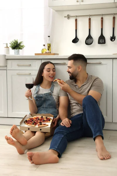 Happy young couple eating pizza and drinking wine in kitchen
